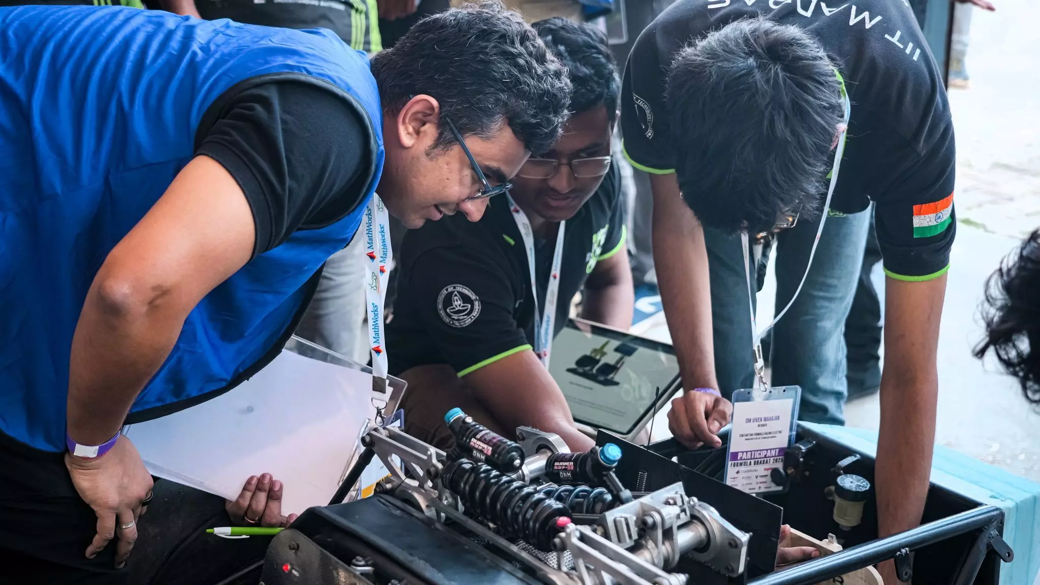 Teammates engaged in a collaborative problem-solving routine, tinkering their hand-built formula racecar
